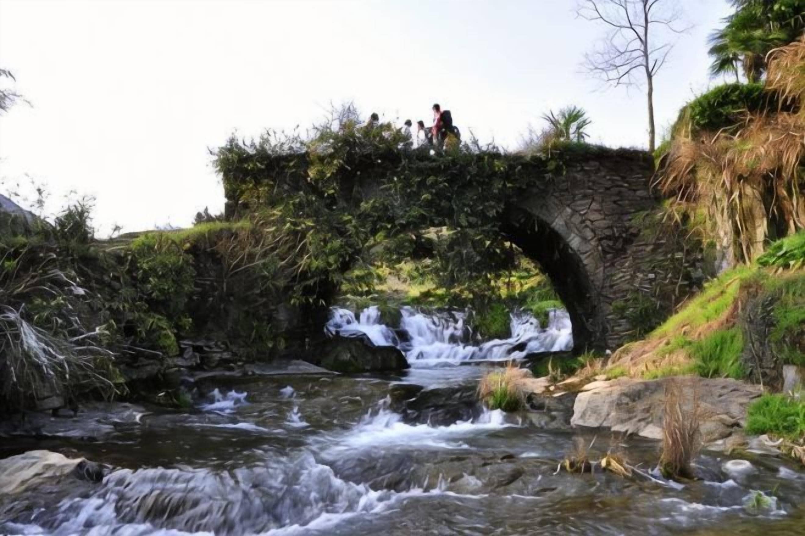 Un puente de piedra sobre un arroyo con personas de pie.