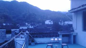 A rooftop terrace with a view of a village, a railing, and two stools.