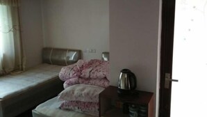 A small, simple room with a bed, a pillow, a bedside table with a kettle, and a window with curtains. - Qingyuan Renjia Inn (Wuyuan)