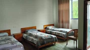 A room with three single beds, a wooden chair, and a window with curtains.