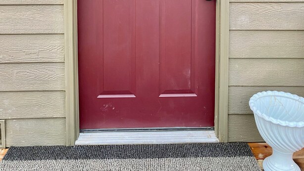 A red door with a heart-shaped wreath, a mailbox, and a light fixture on the wall. - Quaint Cottage @ Fort Nibbe  (Worden)