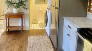 A compact kitchen with a washing machine, a small table with a plant, and a refrigerator. - Quaint Cottage @ Fort Nibbe  (Worden)