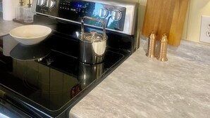 A kitchen with a black stove, a white bowl, a stainless steel pot, and a wooden cutting board. - Quaint Cottage @ Fort Nibbe  (Worden)