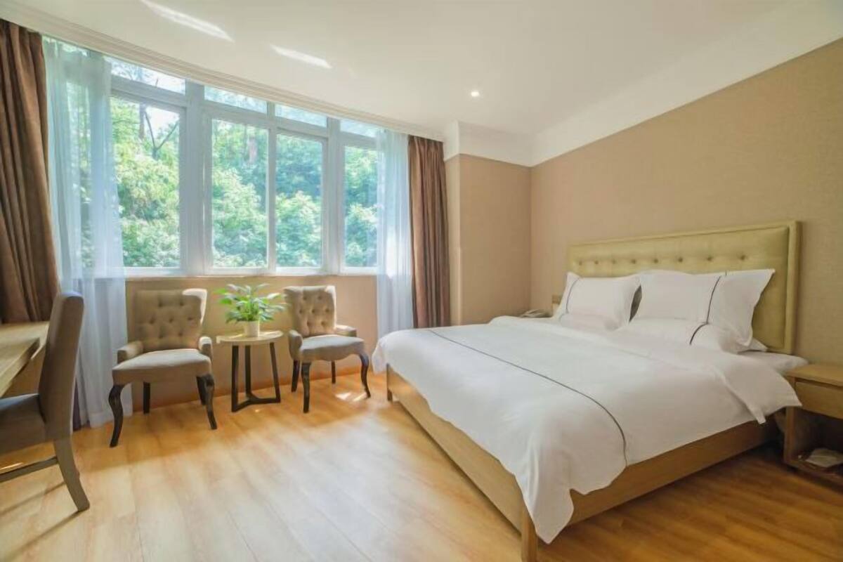 A bedroom with a large bed, a desk, two chairs, and a small table with a plant.