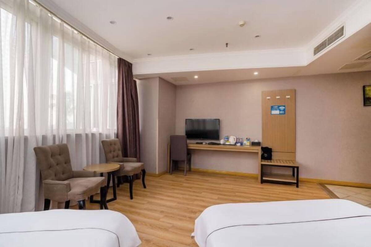A hotel room with two beds, a desk with a TV, a chair, and a small table.