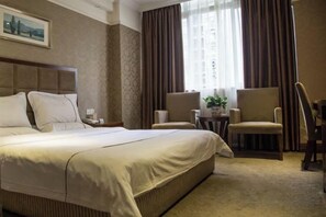 Habitación de hotel con una cama grande, dos sillones, una mesita y un ventanal con cortinas.
