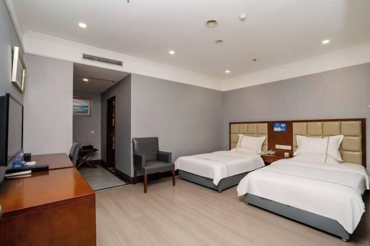 A hotel room with two beds, a desk, a chair, and a television.