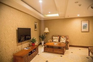 A living room with a flat-screen TV, a sofa, a coffee table, and a lamp. - Chongqing Ba Bai Feng Traders Hotel (Chongqing)