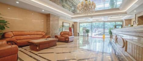A spacious lobby with a high ceiling, a chandelier, a leather sofa, a coffee table, and a marble floor.