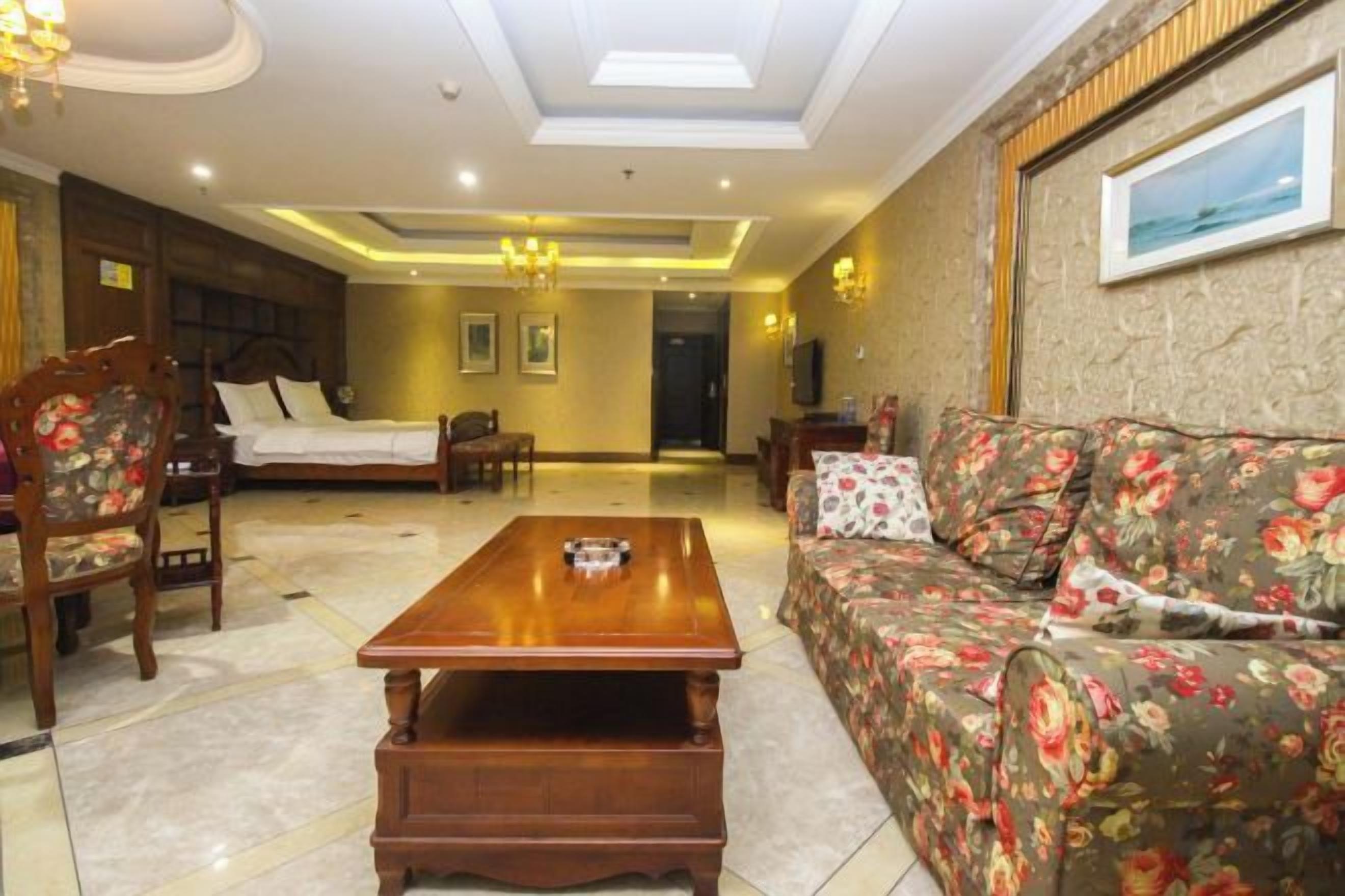 A hotel room with a bed, a sofa, a wooden coffee table, a chair, and a television.