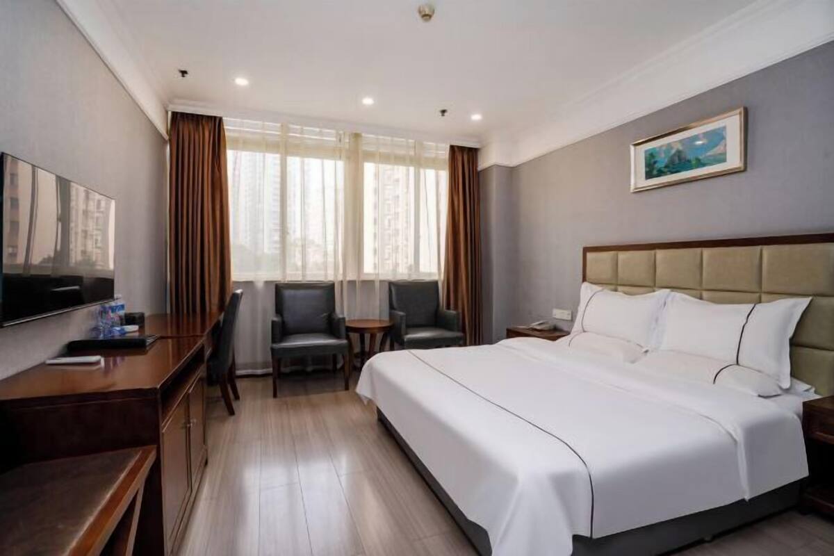A hotel room with a large bed, a desk with a chair, a small table, and a TV.