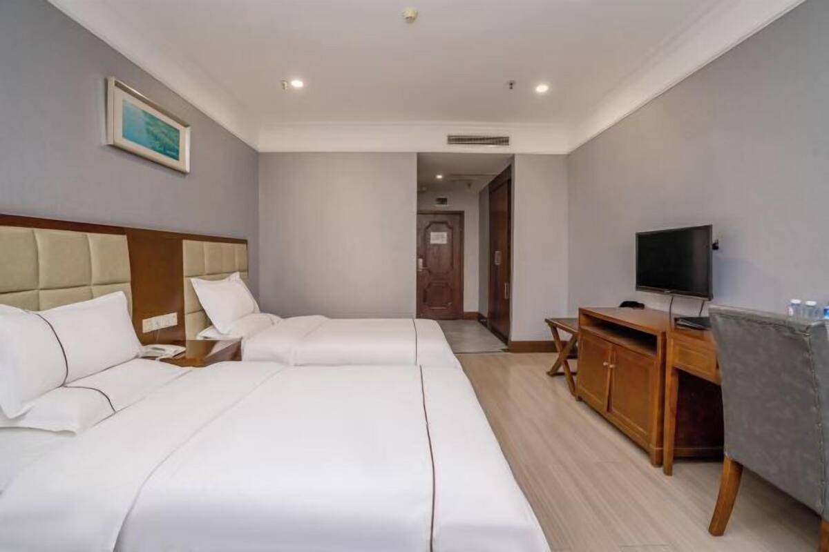 A hotel room with two beds, a TV, a wooden cabinet, and a painting on the wall.