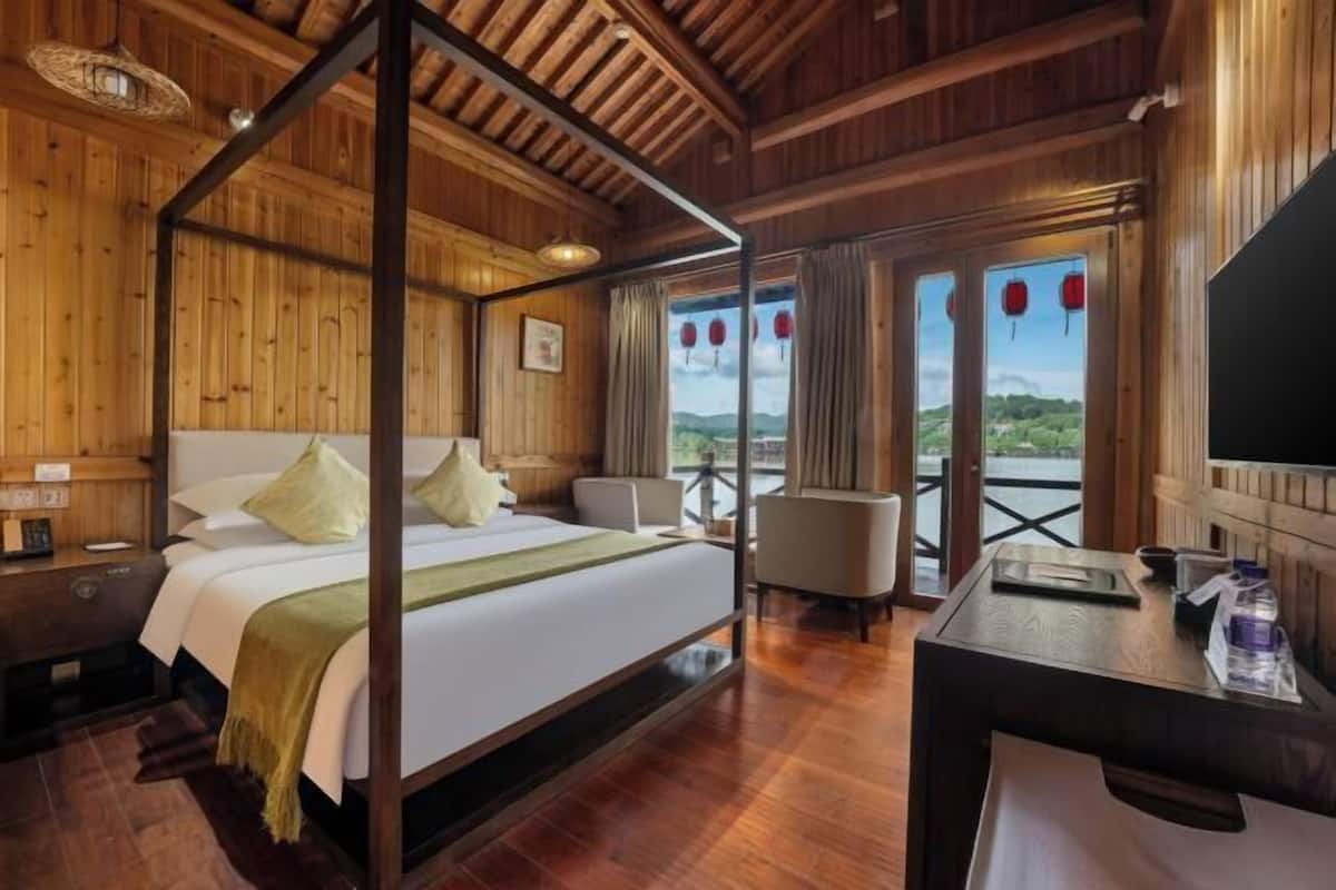 A wooden room with a four-poster bed, a desk, and a view of the outdoors.