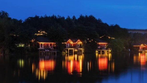 Conjunto de edificios de estilo tradicional con superficies acuáticas reflectantes, probablemente un hotel o resort, con un fondo boscoso.