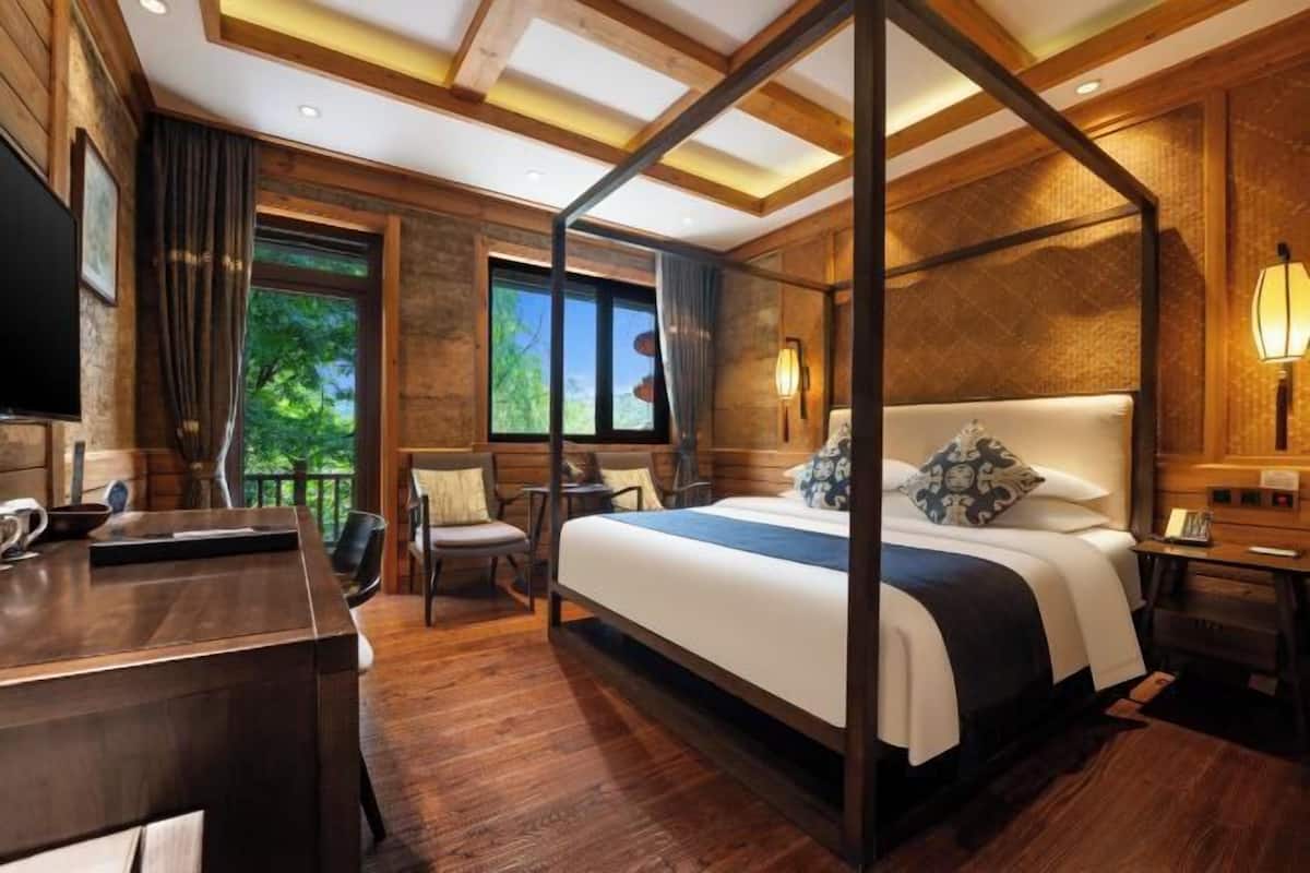A spacious bedroom with a four-poster bed, a wooden desk, and a view of the outdoors.