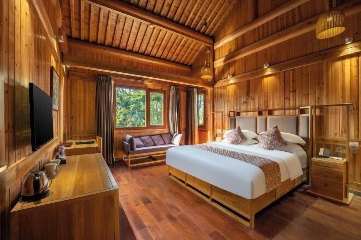 A wooden cabin-style bedroom with a large bed, a TV, a sofa, and a wooden desk.
