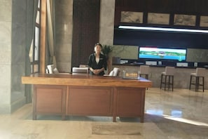 Un mostrador de recepción con una recepcionista, una pantalla de televisión y una zona de estar con sillones.
