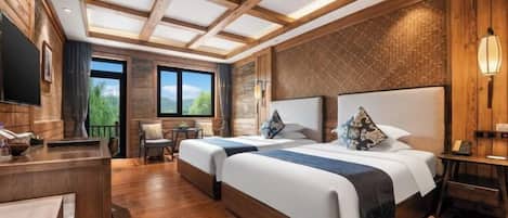 Habitación de hotel con dos camas, piso de madera, un escritorio, una silla y un ventanal con vistas a zonas verdes.