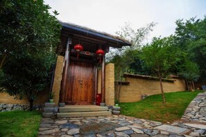 A traditional wooden building with a tiled roof, a stone pathway leading to the entrance, and a brick wall.