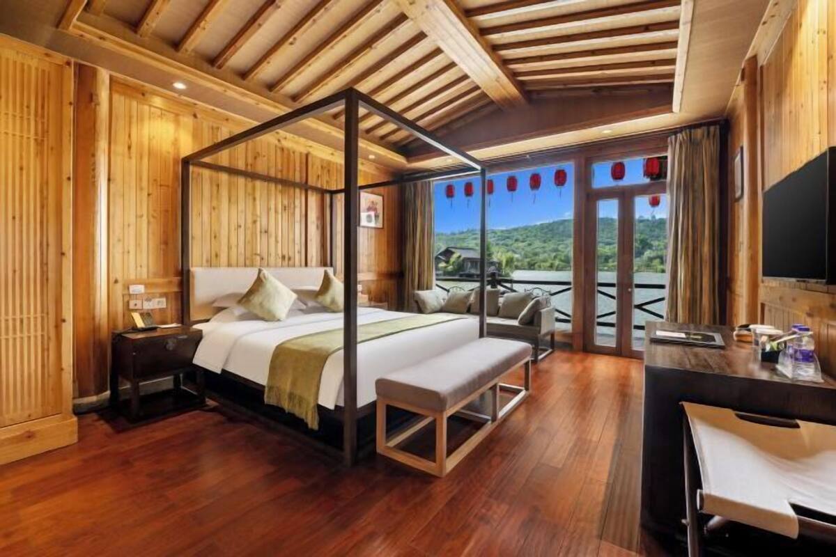 A wooden-paneled room with a four-poster bed, a desk, and a view of the outdoors.