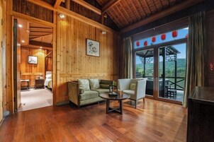 Interior de madera con sofá, sillón y mesa. Se ve el exterior a través de un ventanal.