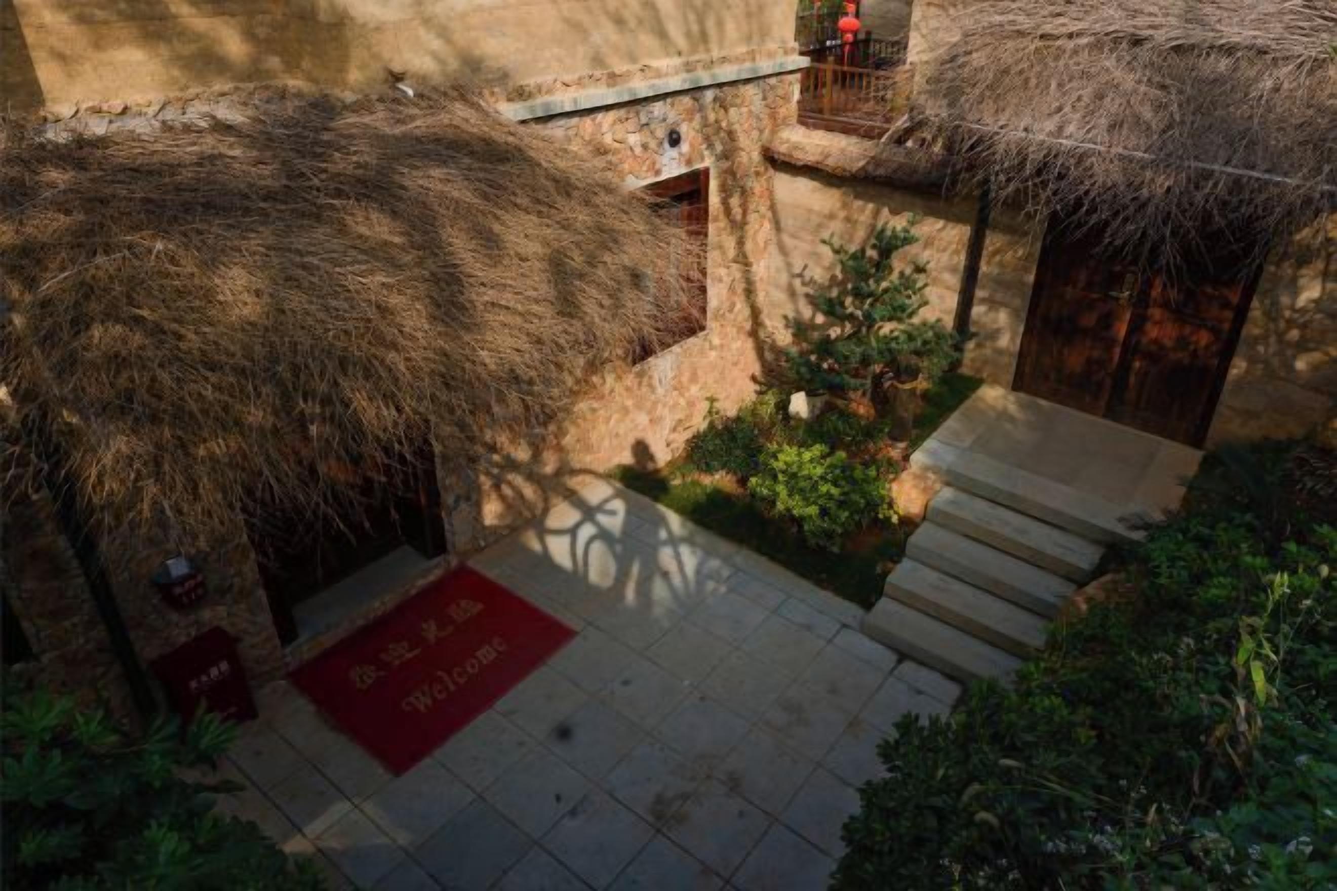 Un patio con una estructura de techo de paja, un tapete rojo y una escalera que lleva a una puerta de madera.