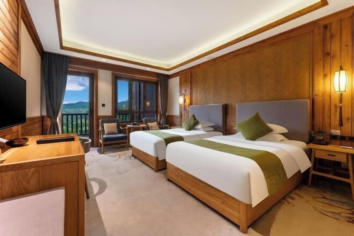 A hotel room with two beds, a desk, a TV, and a balcony with a view.
