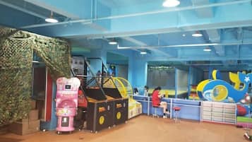 An indoor play area with a climbing wall, a pink arcade machine, and a blue and yellow play structure.