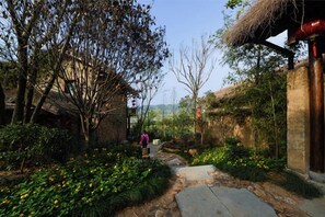 A garden pathway with a stone bench, surrounded by greenery and a thatched roof structure. - Gengdu Resort (Jiangshan)