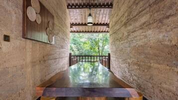 A long wooden table in a rustic room with exposed brick walls and a view of greenery outside.