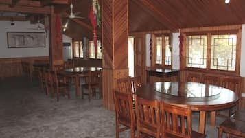 A wooden dining area with round tables and chairs, a ceiling fan, and windows with bars.