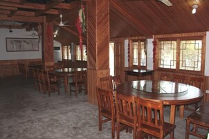 Un comedor de madera con mesas y sillas redondas, un ventilador de techo y ventanas con barrotes.