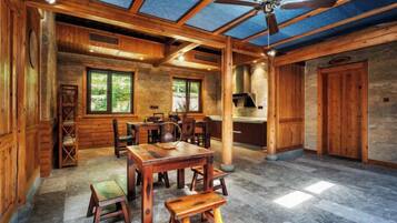 A spacious room with a wooden ceiling, a dining table with chairs, a bench, and a ceiling fan.