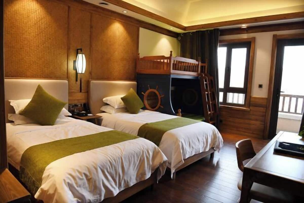 A hotel room with two beds, a wooden bunk bed, a desk, a chair, a lamp, and a window with curtains.