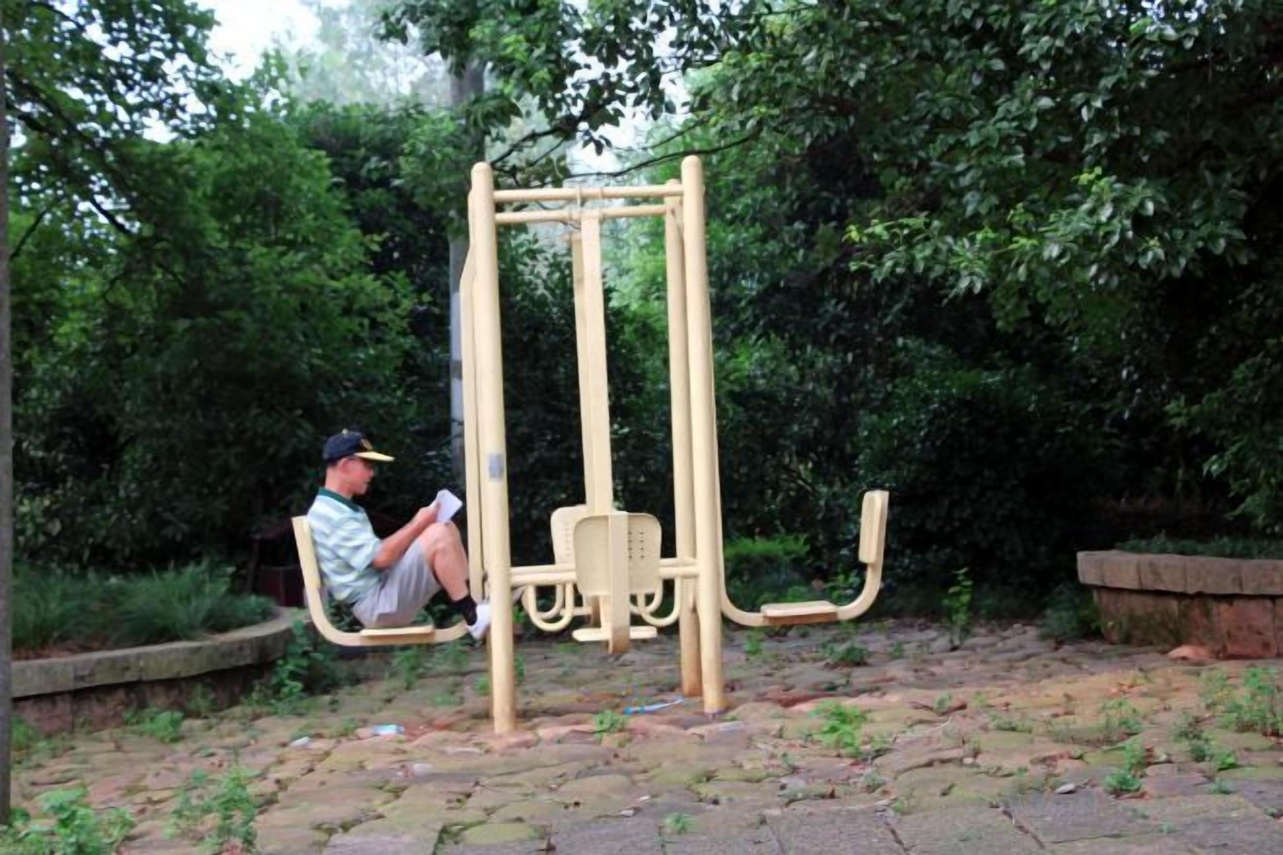 A man sitting on a swing set in a park with greenery in the background.