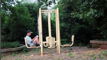 A man sitting on a swing set in a park with greenery in the background.
