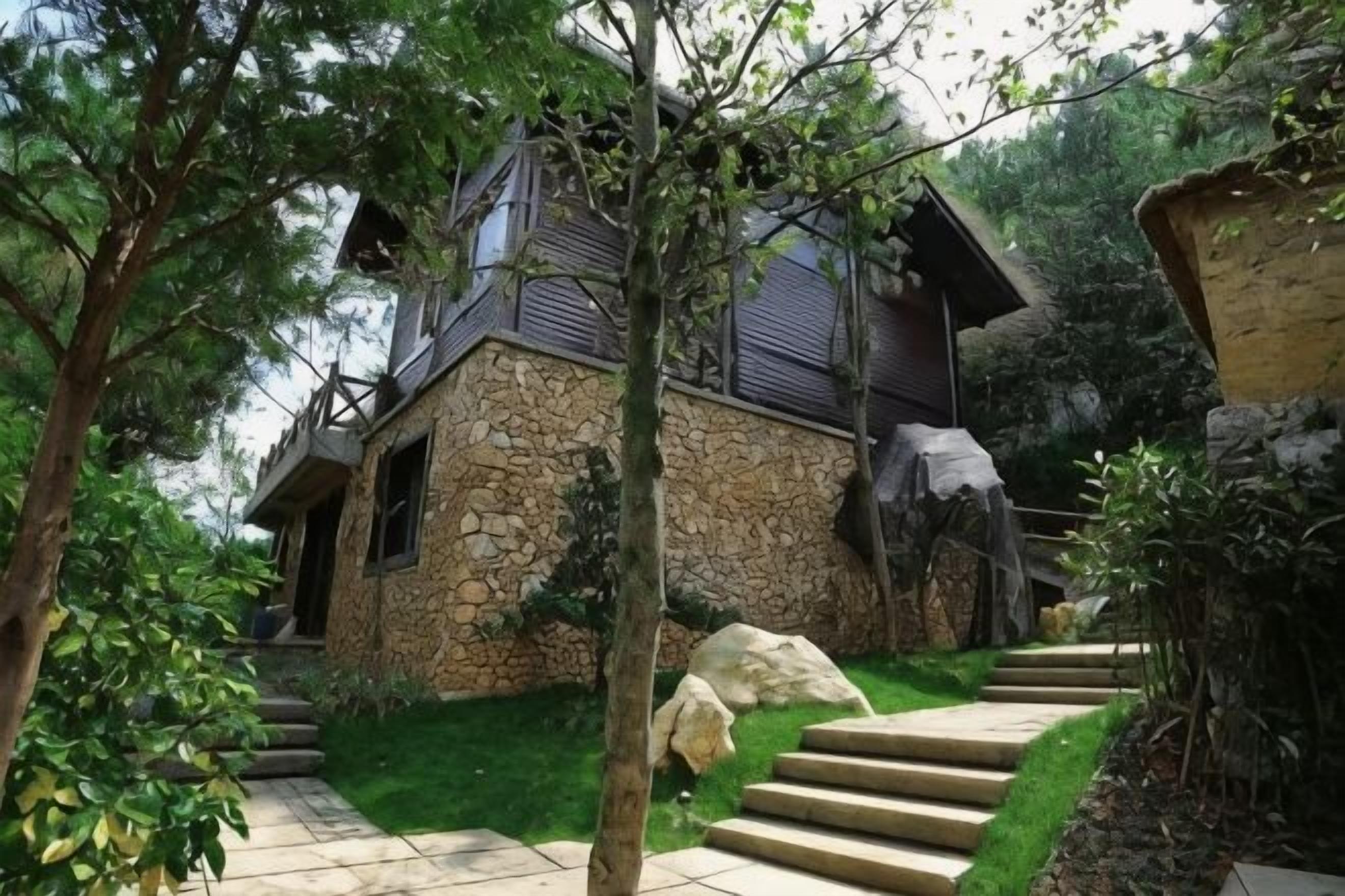 A stone house with a staircase leading to a wooden deck, surrounded by greenery.