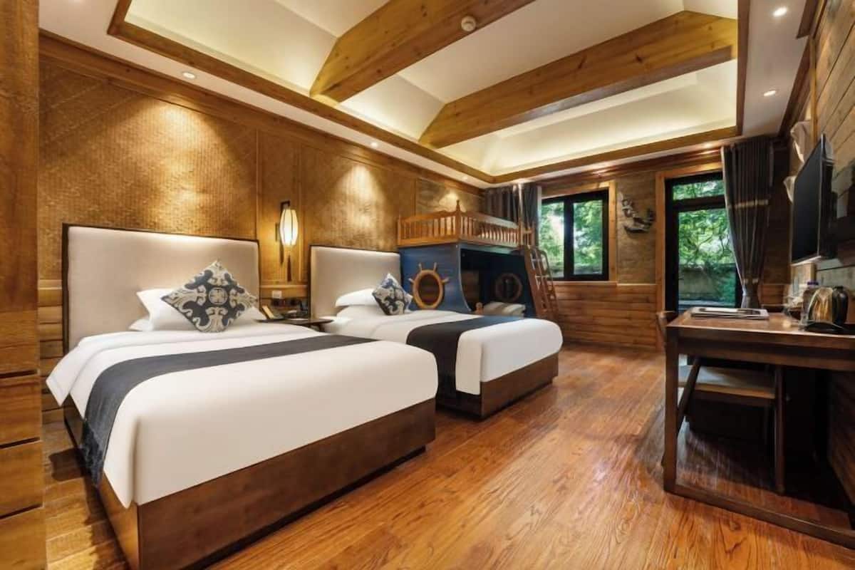 A wooden cabin-style bedroom with two beds, a desk, and a bunk bed.