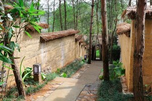 Un sendero conduce a edificios de estilo tradicional con techos de paja, rodeados de abundante vegetación.