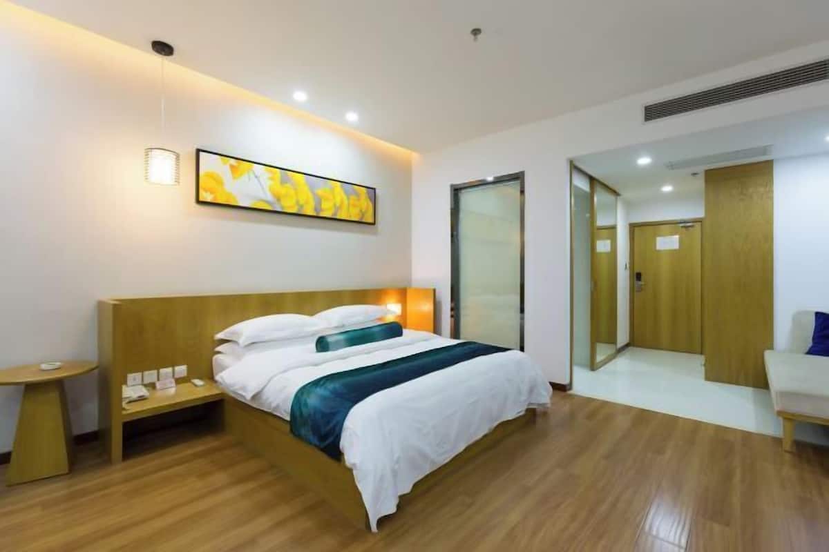 A hotel room with a wooden bed, bedside table, and a wall-mounted artwork.