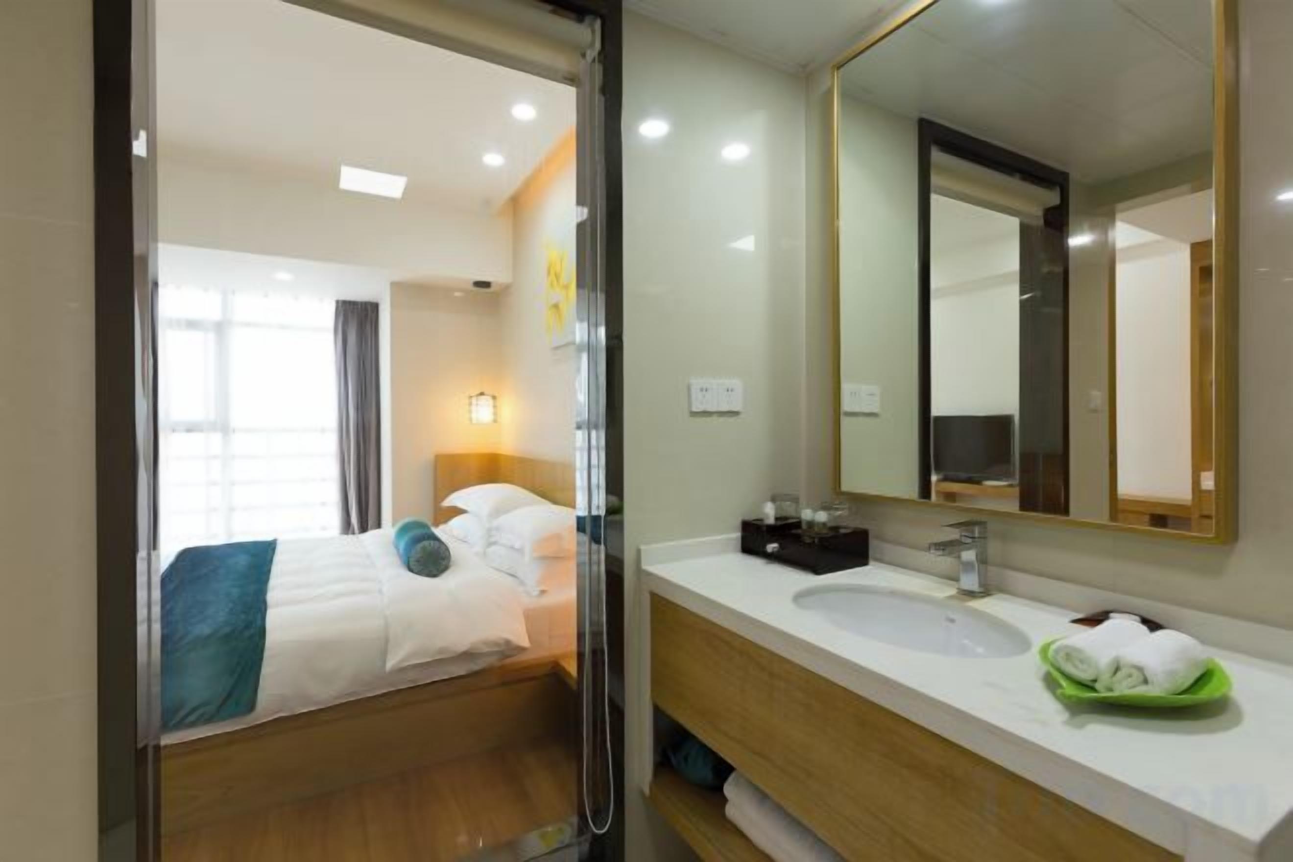 A hotel room with a bed, a bathroom with a sink and mirror, and a view of the outside.