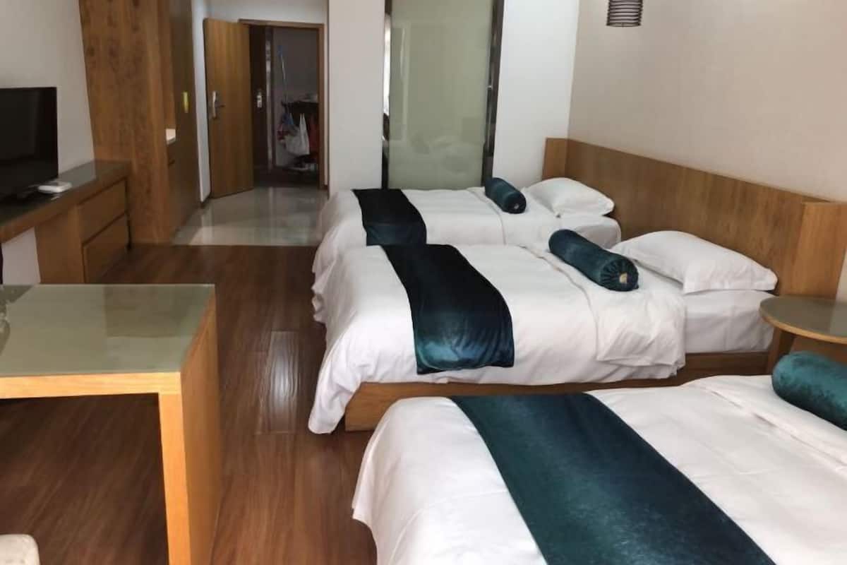 A hotel room with three beds, a wooden desk, and a television.