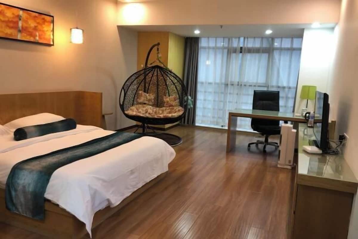 A hotel room with a bed, a hanging chair, a desk with a computer, and a window with curtains.