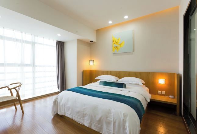 A hotel room with a large bed, a wooden nightstand, a chair, and a window with curtains.