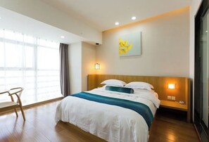 A hotel room with a large bed, a wooden nightstand, a chair, and a window with curtains. - Ginkgo Hotel (Xuzhou)
