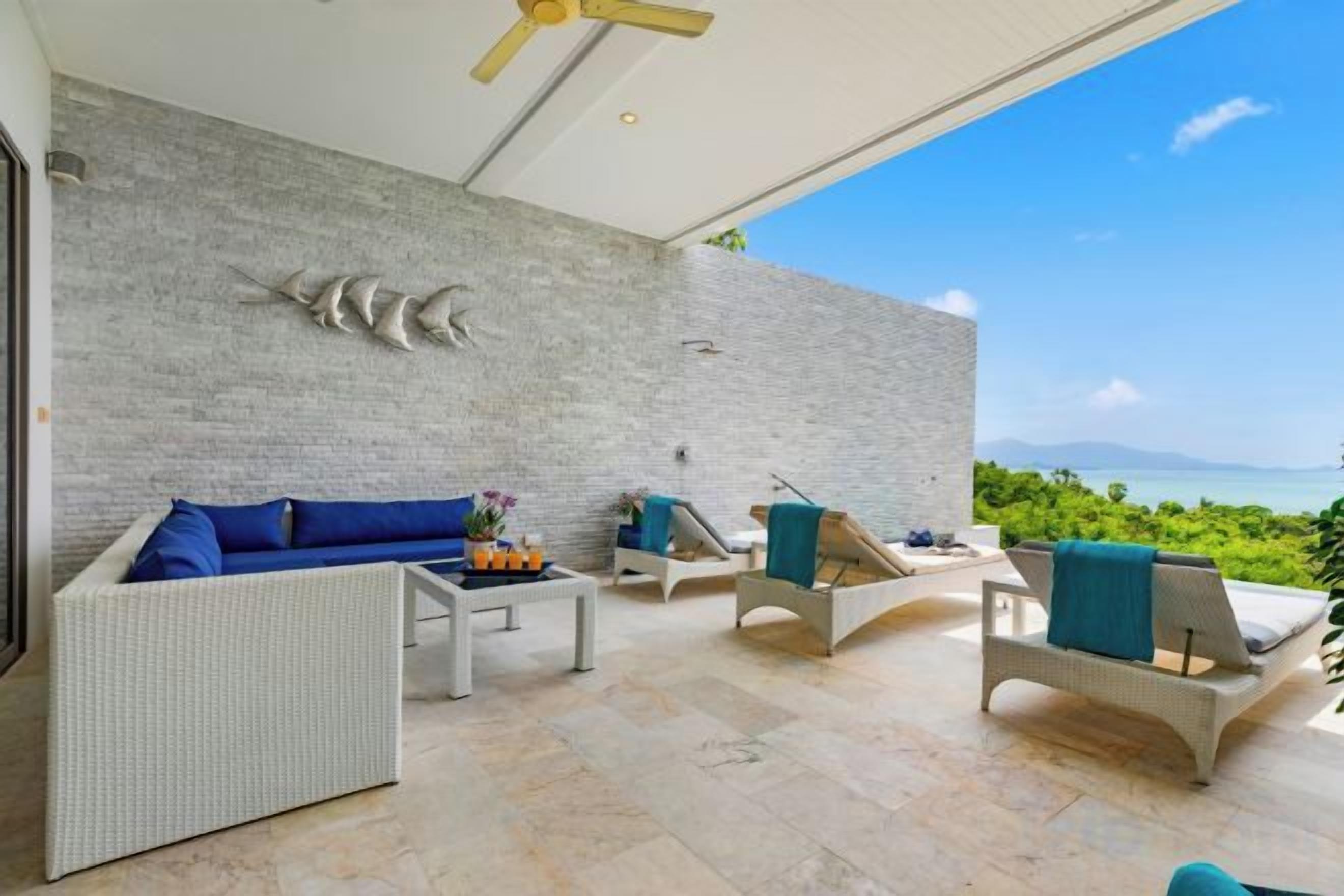 A modern outdoor lounge area with a stone wall, wicker furniture, and a view of the sea.