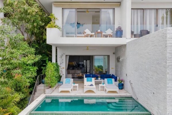 A modern two-story building with a swimming pool, lounge chairs, and a balcony.