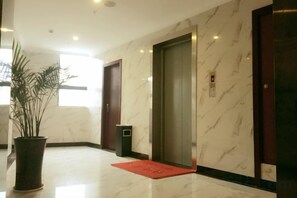 A hotel lobby with a marble floor, a potted plant, a red mat, and an elevator. - lemon hotel (Chongqing)