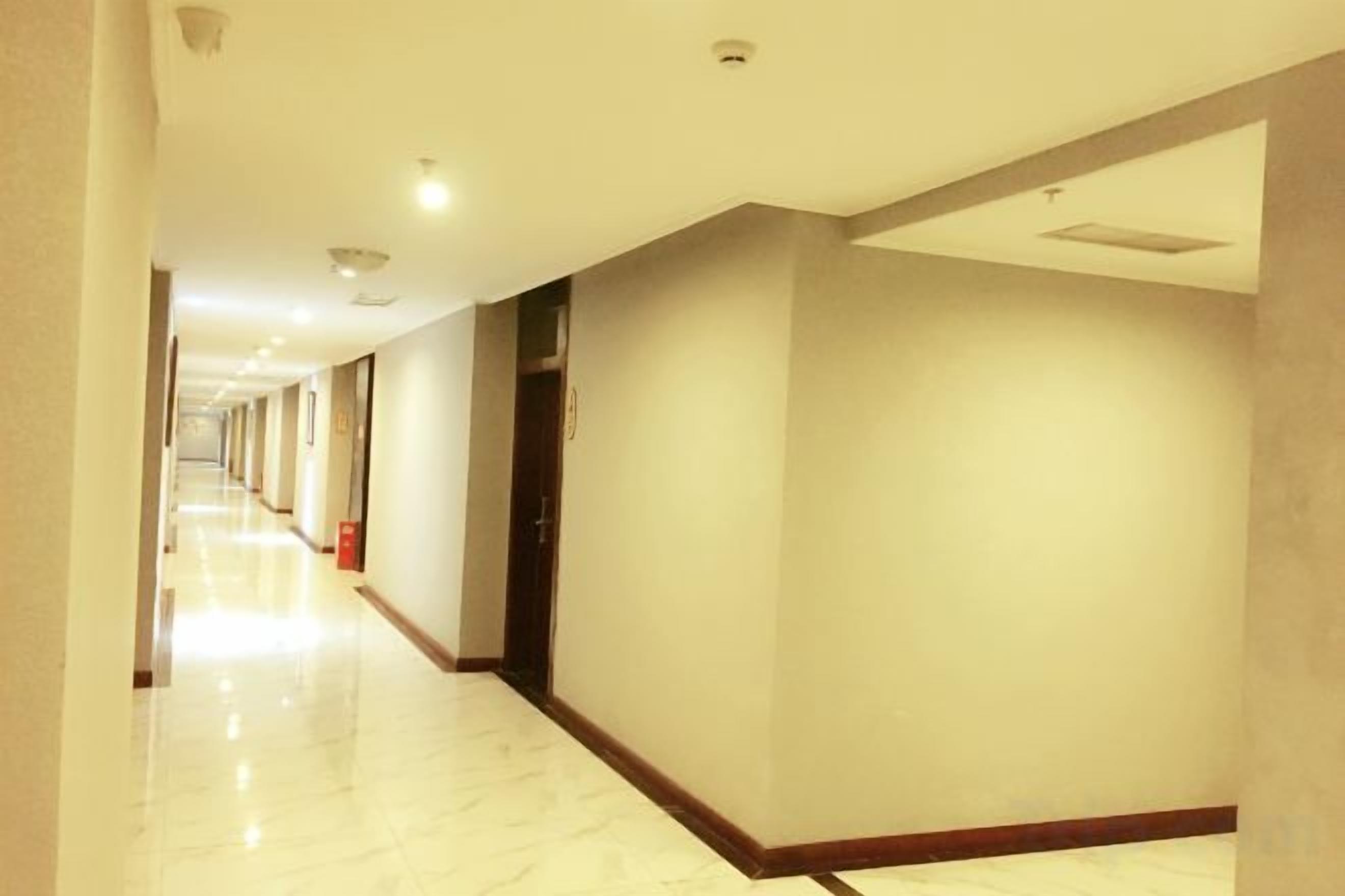 A hotel corridor with a marble floor, doors on the right, and a fire extinguisher on the left.