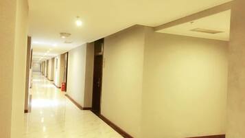 A hotel corridor with a marble floor, doors on the right, and a fire extinguisher on the left.